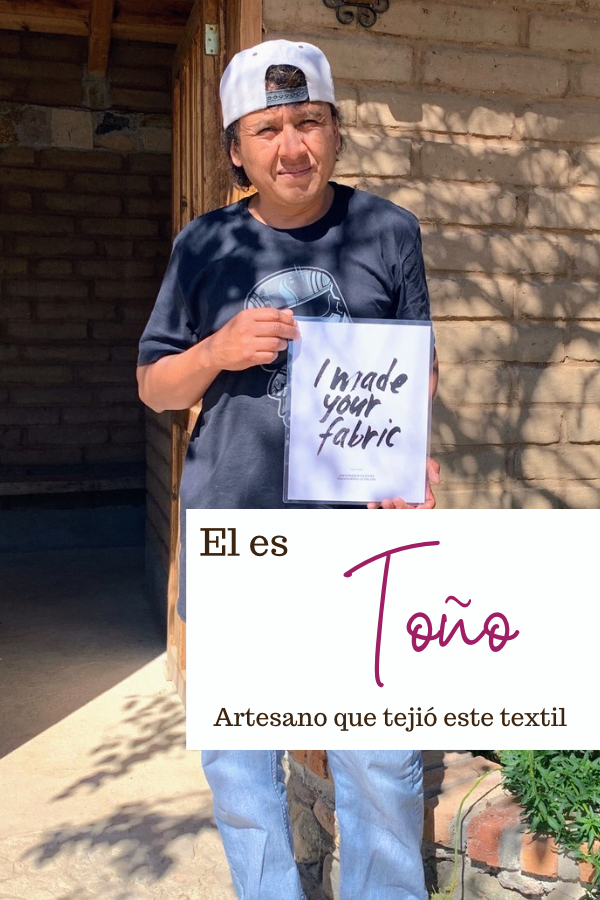 Artesano Antonio mostrando un letrero en el que dice que él hizo el textil con el que se elaboró la prenda de Nativa de Corazón