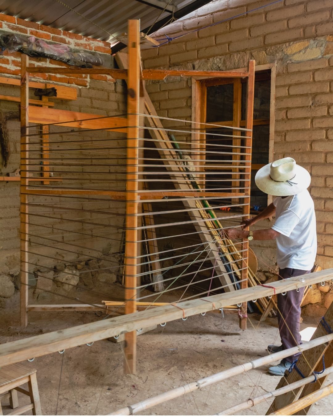 Sr. Antonio, papá de Toño, lo apoya en el acomodo de hilos para la preparación de la base en el telar de pedal. Labor que lleva tiempo, paciencia y conocimiento.